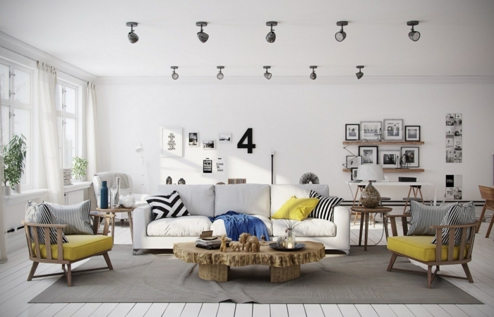 sala de estar grande con mucha luz natural, sofá blanca, cojines amarillos y rayados en blanco y negro, sillones de madera, tarima en el suelo, alfombra gris, decoracion con cuadros, mesa de madera rustica, dormitorio nordico