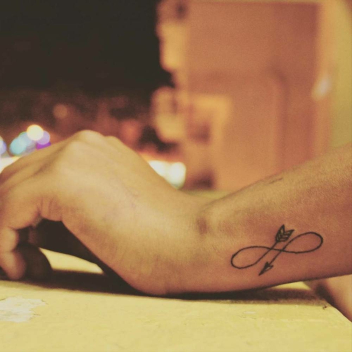 tatuaje combinado de flechas y el símbolo del infinito en la parte lateral de la muñeca, mano de hombre, tattoo en la muñeca