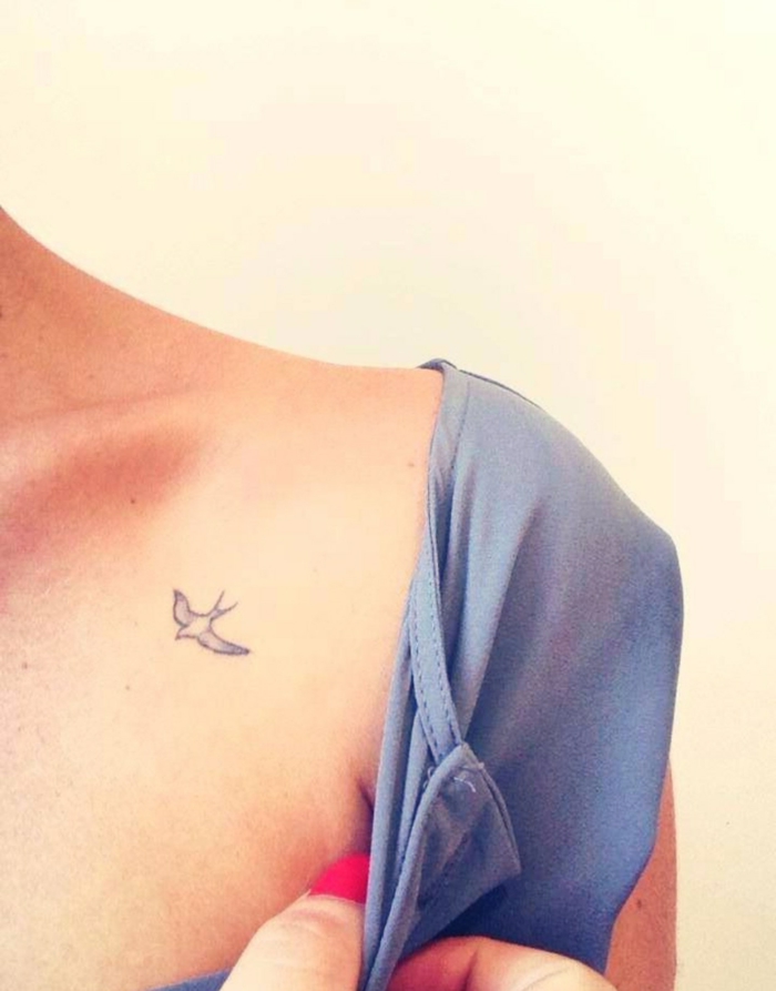 mujer con uñas pintadas y blusa azul, tatuaje pequeño de golondrina volando, tatuaje en la clavicula, tatuajes elegantes