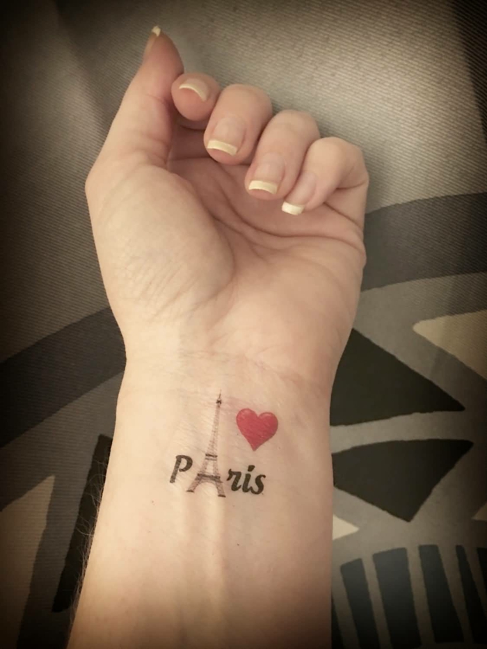 tatuajes muñeca, mano con manicura, tatuaje con el nombre Paris, la torre aifel y corazon rojo, tattoo combinación de imágenes y letras