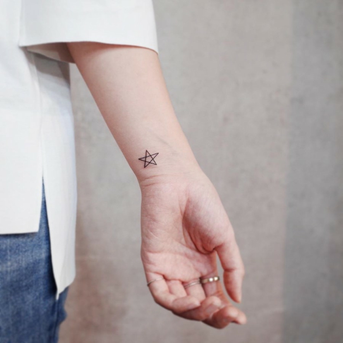 mujer con camisa de mangas tres cuartos y anillos, tatuaje minimalista en la muñeca, estrella de cinco puntos, tatuajes pequeños para mujeres originales