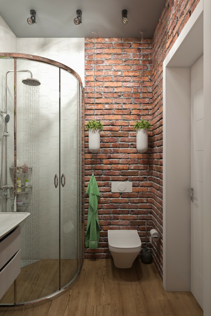 decoracion baños pequeños, pared de ladrillo visto con macetas colgantes blancas, cabina de ducha en el ángulo, suelo de madera, colores contrastes
