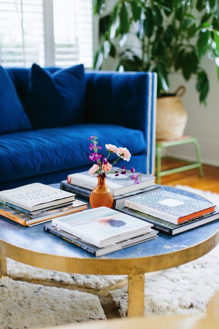 mesa redonda baja con revistas, estilo nórdico, muebles escandinavos, sofá de terciopleo azul, planta verde, alfombra blanca