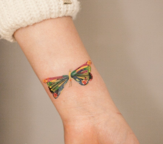 tatuaje de mariposa de colores, rojo, amarillo y verde, mujer tatuada muñeca, jersey blanco, tatuajes pequeños originales, 