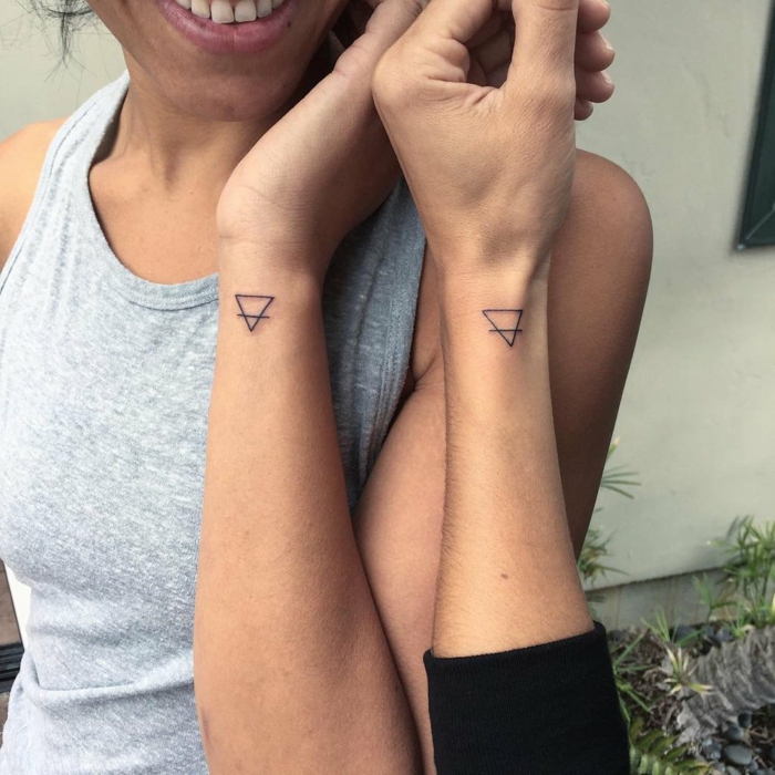 tatuajes iguales en la muñeca, diseño geométrico, triángulos invertidos cruzados por una línea, simbolo de familia, mujer con blusa gris y sonrisa