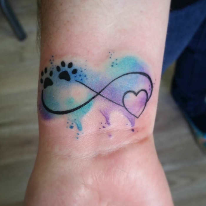 tatuaje combinación del símbolo del infinito con coraón y huellas de perro, mancha de color tipo acuarela en azul y lilá, tattoos pequeños