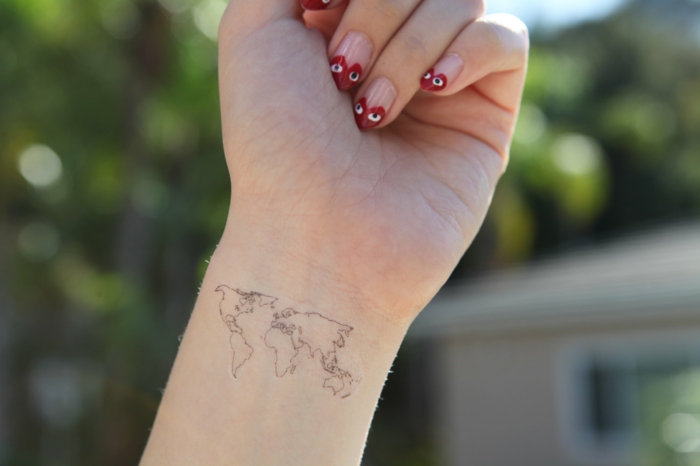mano de mujer con manicura en rosa y rojo, tattoos pequeños, tatuaje minimalista delicado mapa mundo, 