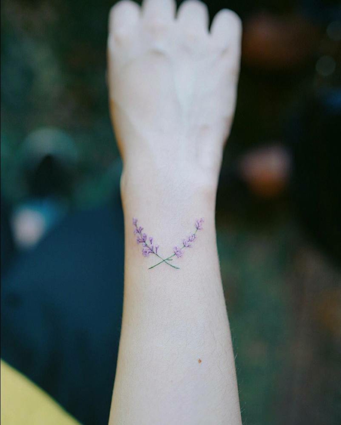 diseño femenino, tatuaje con hojas de lavanda cruzados en la parte exterior d e la muñeca, color verde y lilá, tatuajes originales
