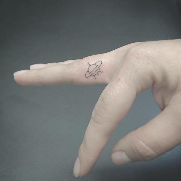 tatuajes en los dedos, mano con piel muy blanca, tatuaje de ovni en el dedo corazon, tatuajes elegantes