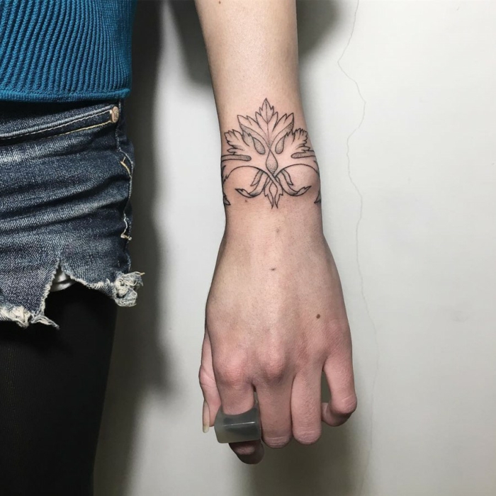 mujer con jeans cortos, mano con anillo, tatuaje en la muñeca delicado con motivos florales tipo brazalete, tatuajes de nombres en la muñeca, 
