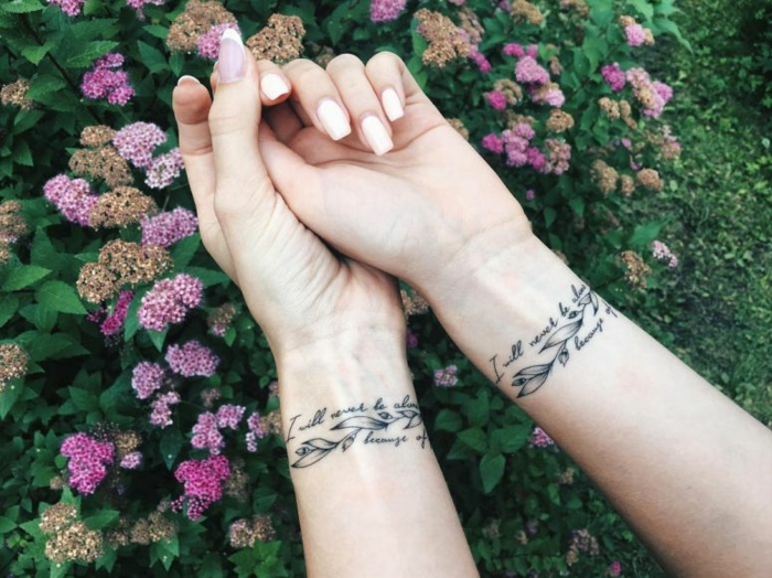 simbolo de familia, tatuajes de hermanas iguales en la muñeca, frase en cursiva y hojas de flores, manos femeninas con manicura, flores en rosado