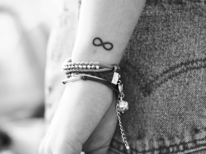 foto en blanco y negro, mujer con jeans y pulseras, tatuaje símbolo del infinito negro, tatuajes en la muñeca