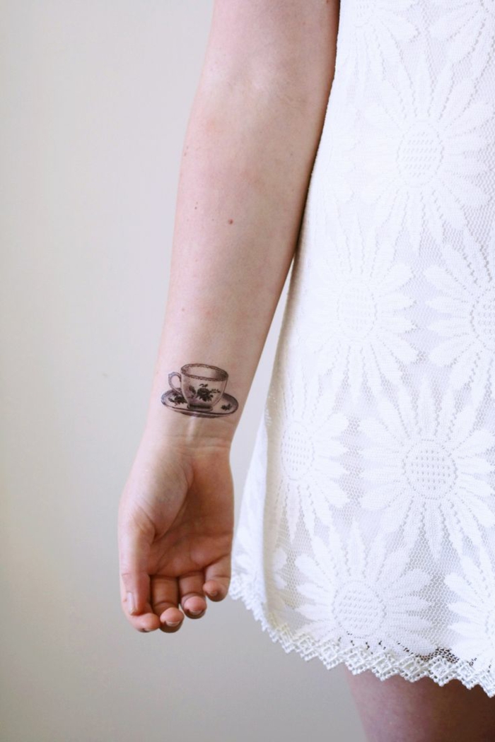 diseño tatuaje divertido, mujer con vestido blanco corto, taza de té en la muñeca, blanco y negro, tatuajes flechas