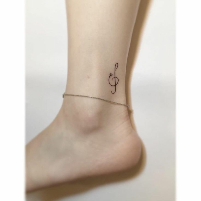 tatuajes chicos, pierna de mujer con pulsera de plata, tatuaje pequeño en el tobillo, clave sol, tattoo femenino