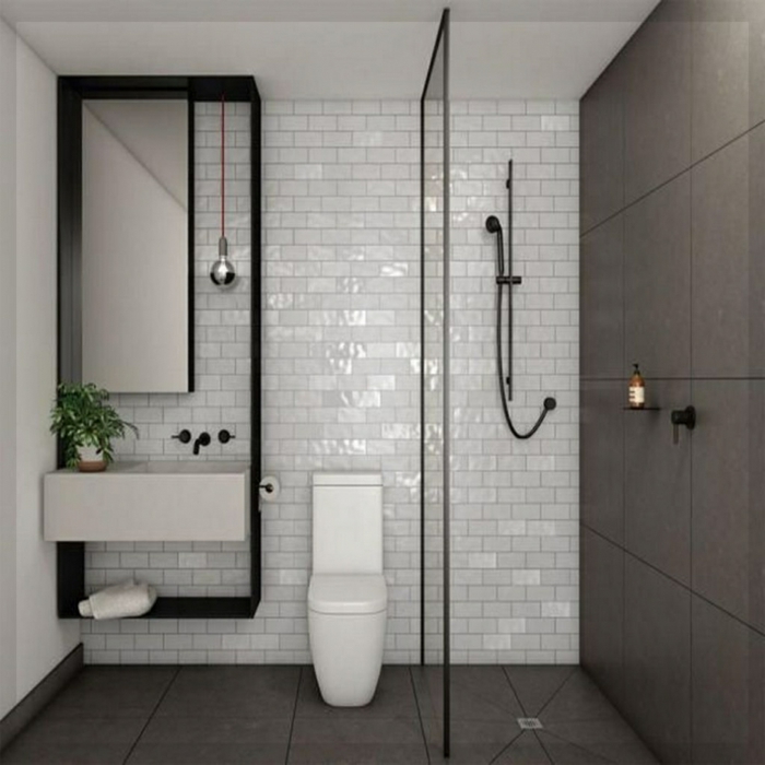 cuartos de baño pequeños, decoracion en blanco y negro con pared de ladrillo visto esmaltado, baldosas en gris pizarra, ducha con mámpara de vidrio, bombilla colgante y planta verde