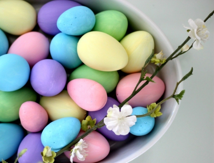 huevos de encanto pintados en colores pastel, huevos coloreados en azul, lila, amarillo y rosado, decoración con ramos de árboles 