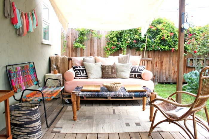 bonita decoración de jardín con muchos elementos decorativos y sillones con palets, sofá en color rosa con cojines coloridos
