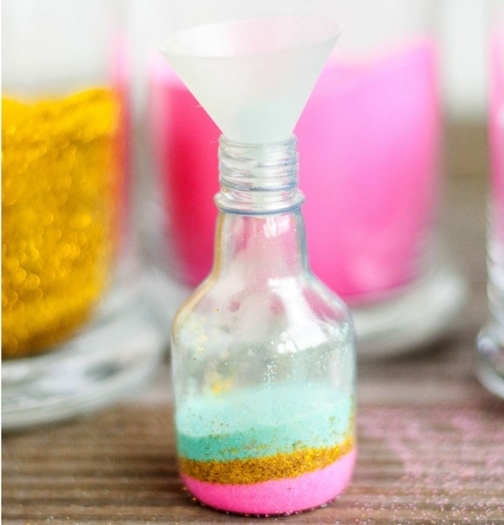 ingeniosas ideas sobre manualidades con botellas de cristal, botella de vidrio de pequeño tamaño llena de purpurina en diferentes colores 