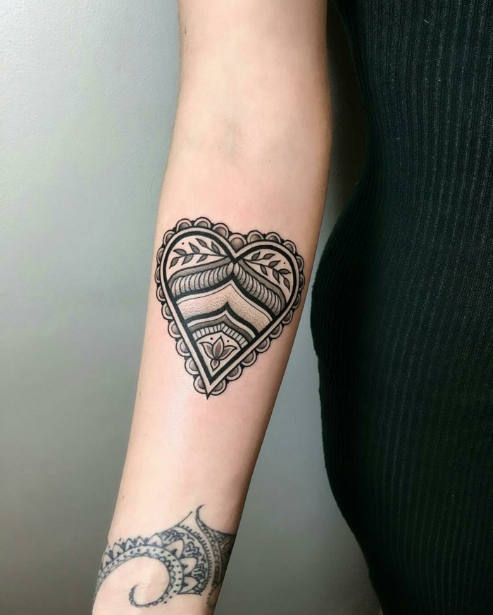 ideas de tatuajes para mujeres en el brazo, tatuaje llamativo con tinte negro en forma de corazón ornamentado con elementos florales 