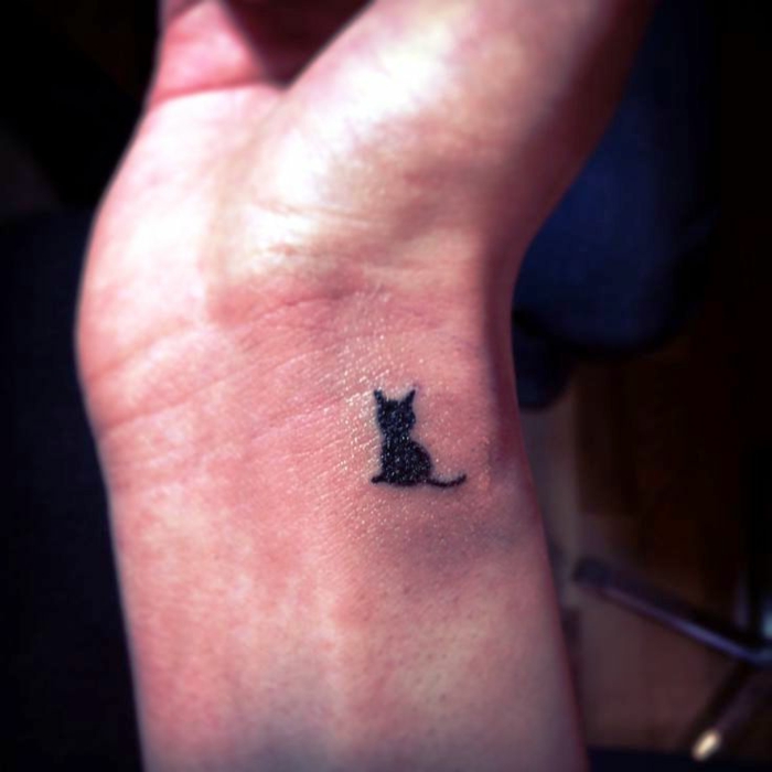tatuaje pequeño de encanto en forma de un gato, pequeño detalle dibujado en la muñeca en negro, ideas tatuajes de mujer