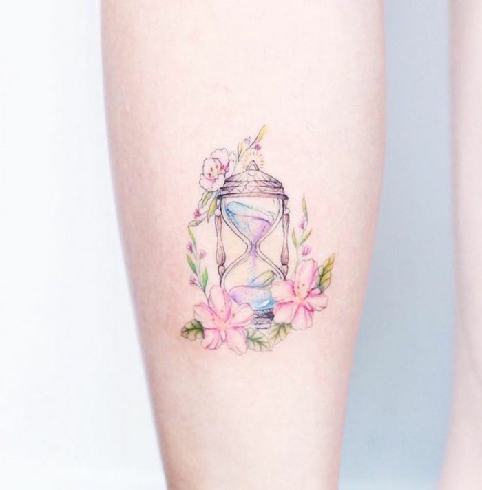 diseños de tatuajes bonitos en acuarela, pequeño tatuaje en la mano de un reloj arena decorado de flores en rosado 