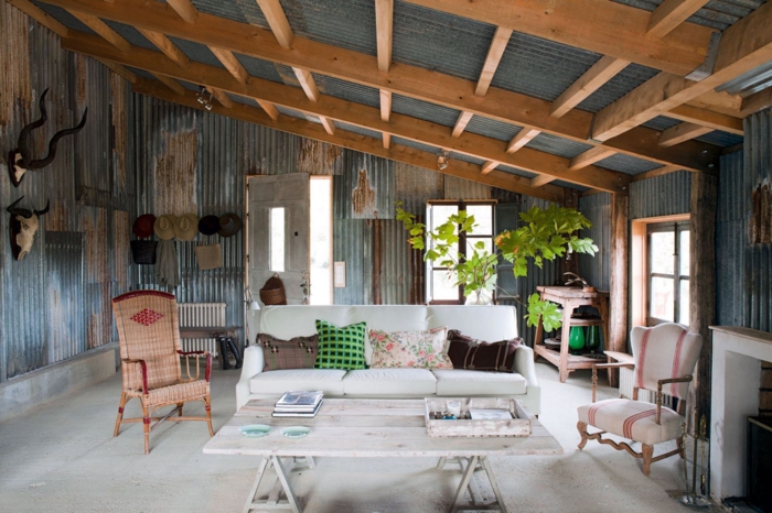 decoracion de salones rusticos, salon con techo inclinado con vigas de madera, paredes con efecto desgastado, sofa en blanco 