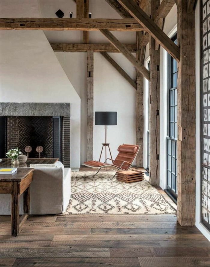 salon con techo alto y paredes en blanco y vigas de madera, alfombra ornamentada y sofá moderna en gris