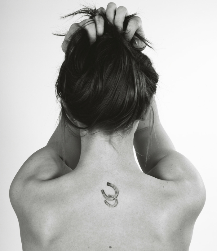 dos herraduras tatuadas en la espalda de la mujer, tatuajes nuca mujer con significado en blanco y negro 