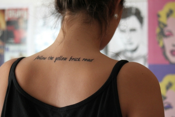 ideas tatuajes en el cuello mujer, tatuaje con letras en tinte negro tatuado en la parte superior de la espalda
