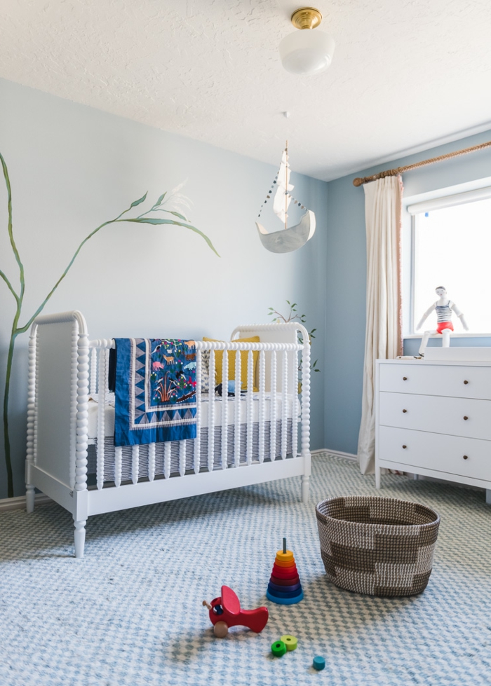 ambiente de encanto decorado en azul celeste, cama de bebé de madera pintada en blanco, suelo con moqueta en cuartos en blanco y azul 