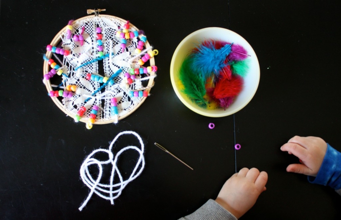 ideas creativas de manualidades para niños, hilo blanco, aguja, aro de madera de crochet, plumas artificiales coloridas