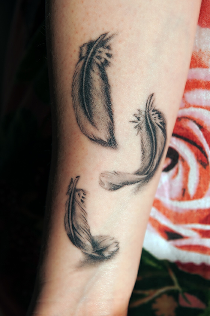 ejemplos de tatuajes pequeños para mujer con plumas, tatuaje en el brazo, tres plumas con tinte negro 