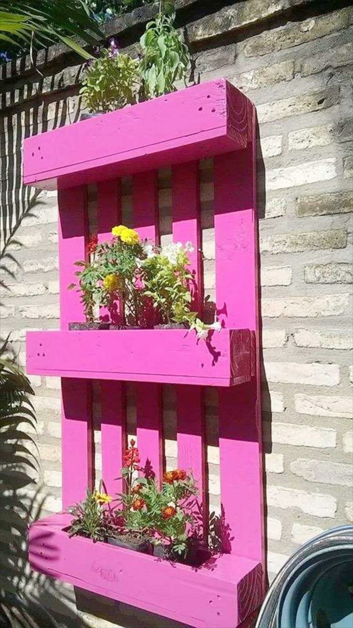 jardin vertical con palets pintado en rosado y colgado en la pared, pequeñas macetas colocadas en los estantes 
