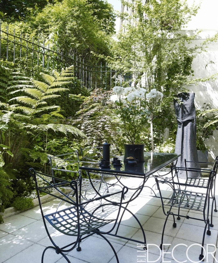 patios ideas para jardines pequeños, sillas y mesa negros de metal, plantas y arbustos altos 