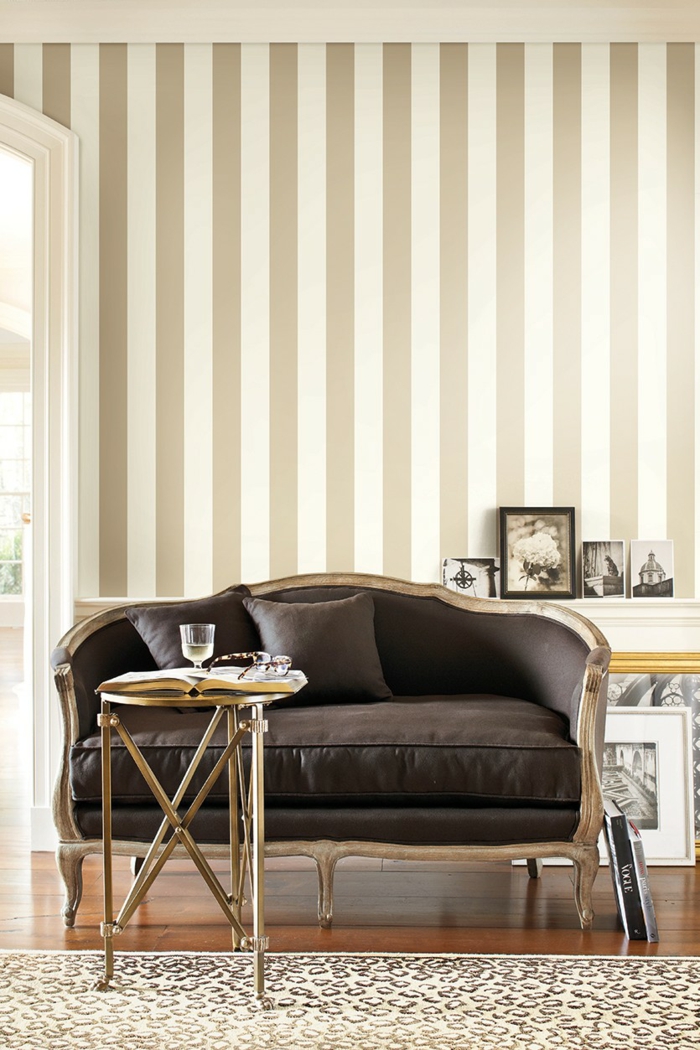 papel decorativo para pared en beige y dorado, sofá en color marrón con borde en dorado, suelo de parquet y mesa pequeña en dorado 