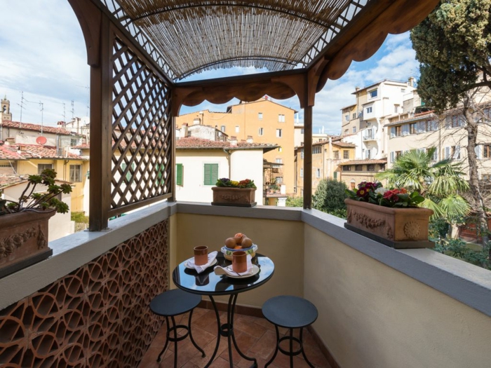 bonita terraza con poca decoración y macetas vintage de arcilla con flores, pequeños muebles en negro 