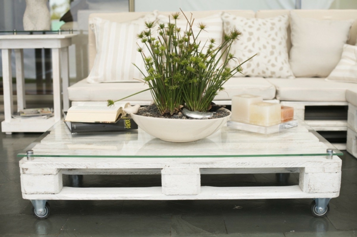 mesa con palets pintada con pintura blancay con vidrio sobre ella sujeto con elementos metálicos