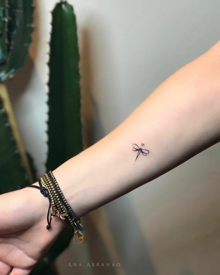 tatuajes pequeños mujer con símbolos, pequeño detalle en el antebrazo, pequeña libélula con tinte negro 