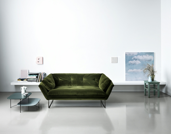 decoracion salon pequeño con sofa de terciopelo en color verde oliva con mesas pequeñas y bajitas y suelo gris clarito
