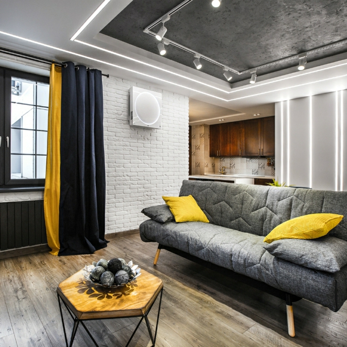 decoracion salon pequeño, sofa gris con cojies en color mostaza con mesa de madera y hierro y cortinas en negro y mostaza