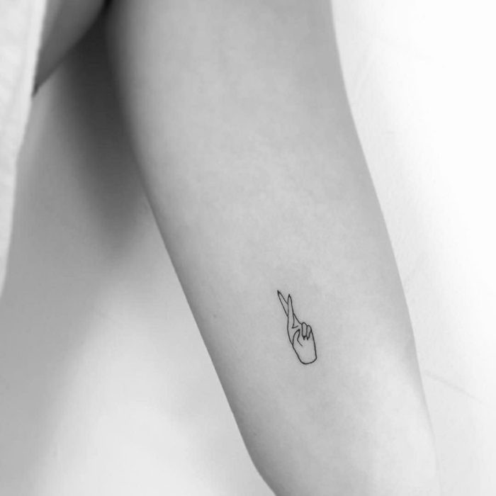 tatuajes en el brazo pequeños con alto simbolisto, mano con dos dedos cruzados, simbolo de la suerte 