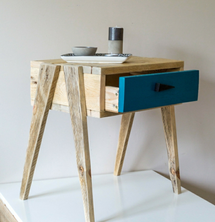 mesa pequeña de palets con patas de madera y con cajón pintado de azul, con vela encima de ella
