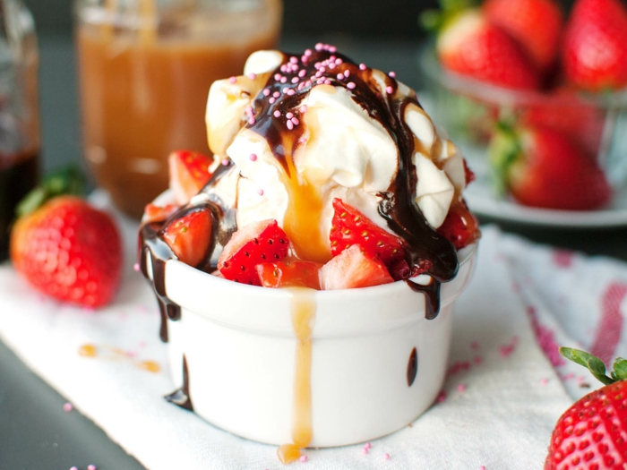  helado de nata con glaseado de chocolate y caramelo y frutos de fresas, postres frios en la mesa servidos