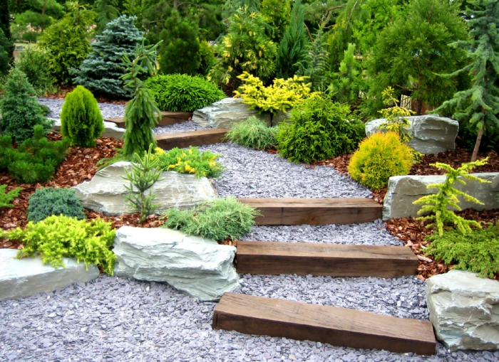 bonito jardín con suelo decorado con gravas en colores gris, escaleras de madera y mucha vegetación 