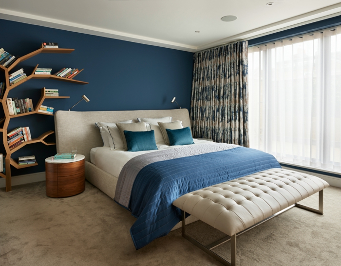 estanterías originales para decoracion dormitorios, grande cama en beige, pie de cama en capitoné y pared en azul intenso 
