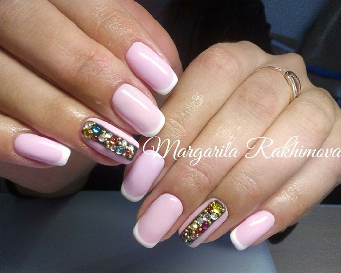 largas uñas en rosado pastel con línea blanca delgada y decoración de cristales coloridos en el dedo anular