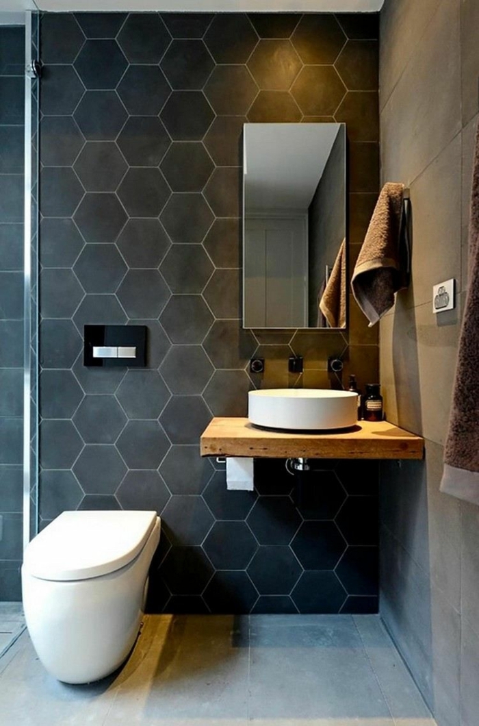 alicatar baños, azulejos hexagonales de color negro en una pared, suelo de color gris, toalla marrón