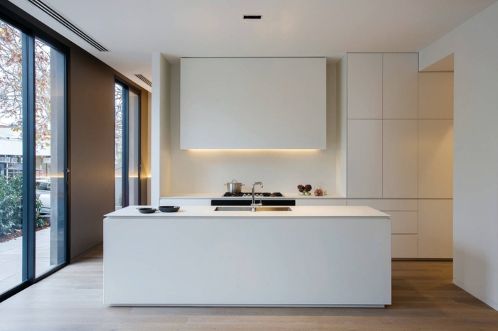 cocinas modernas blancas decoradas en estilo minimalista, muebles de líneas limpias en blanco, suelo de parquet y grandes ventanales 