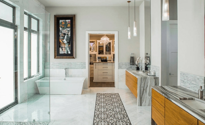 grande baño con bañera moderna en blanco, alfombra ornamentada blanco y gris, cabina de cucha con vitrina de vidrio 