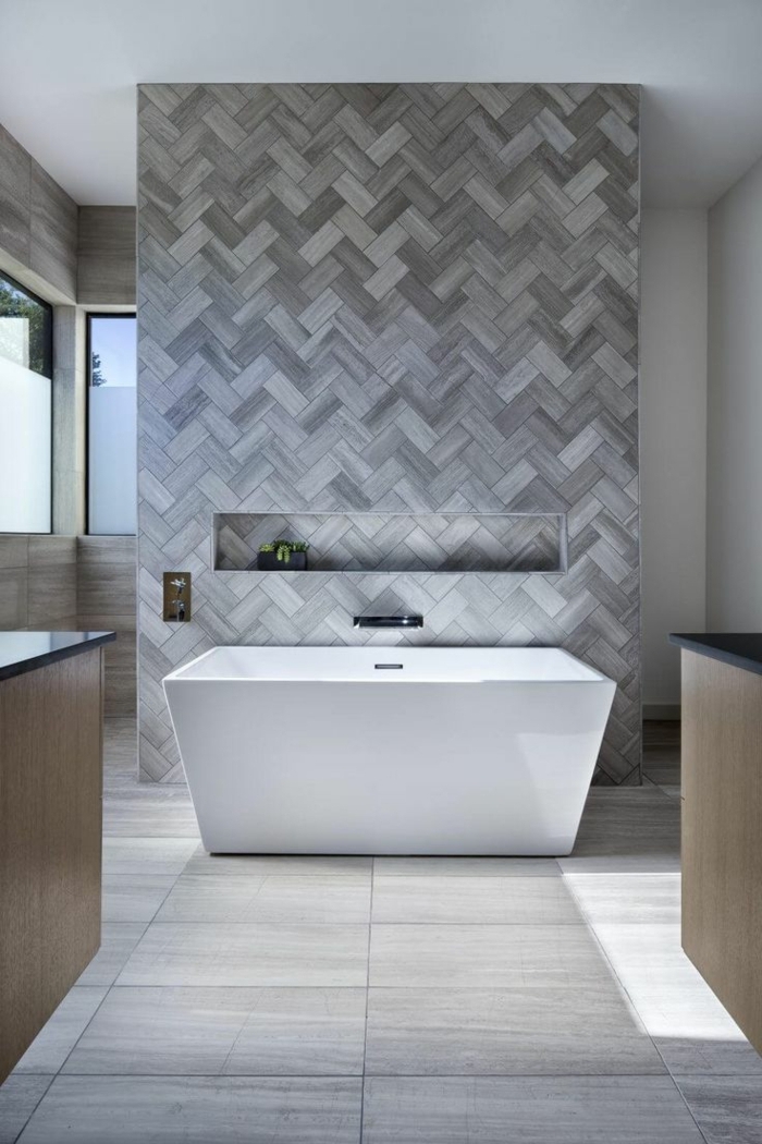 azulejos de baño, una pared con baldosas en diferentes tonalidades del gris, bañera blanca, suelo gris